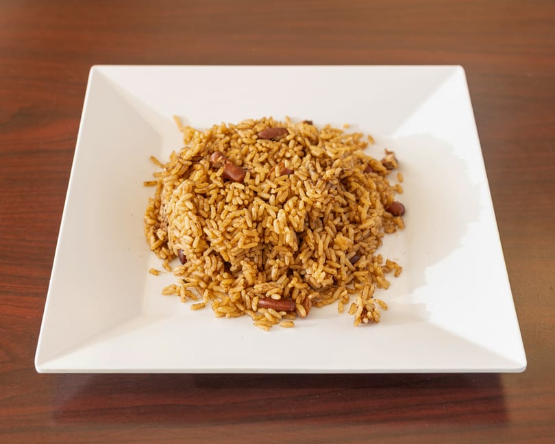 A white square plate filled with seasoned rice and kidney beans on a wooden table.