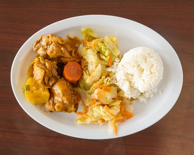 Curry chicken with potatoes and carrots, steamed cabbage, and white rice on a white plate.
