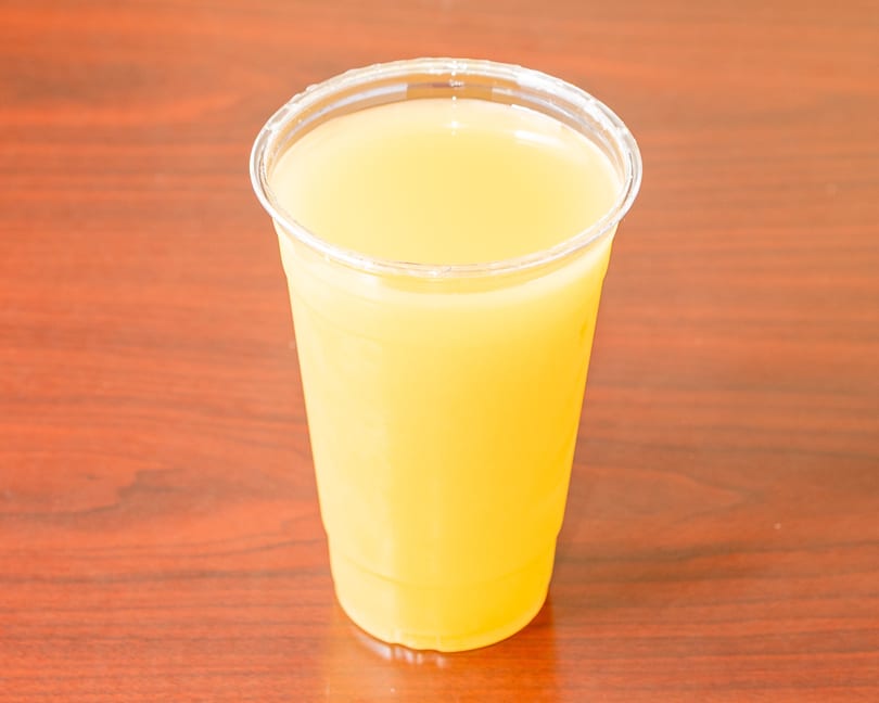 A clear plastic cup filled with bright yellow juice sits on a dark wooden table.