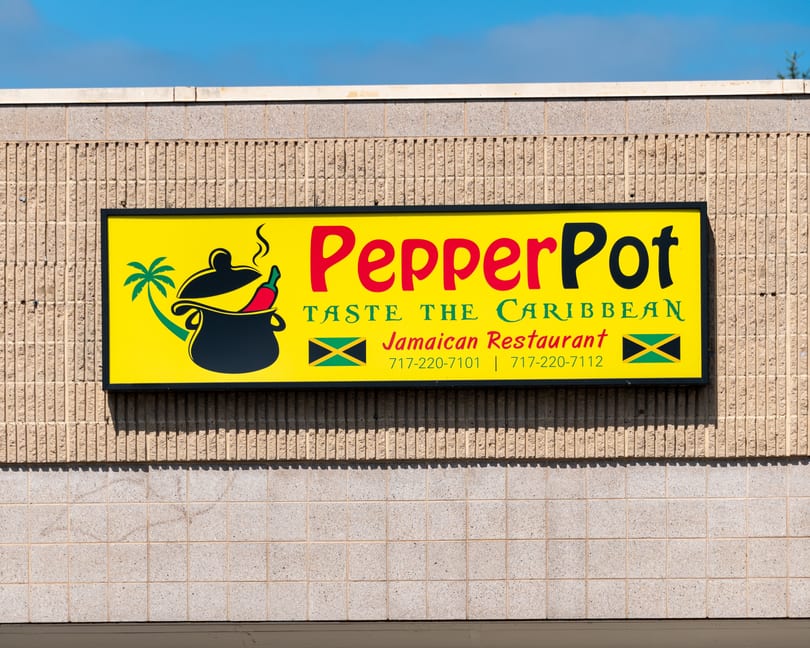 Bright yellow PepperPot Jamaican Restaurant sign with a cooking pot, chili, and palm tree logo.