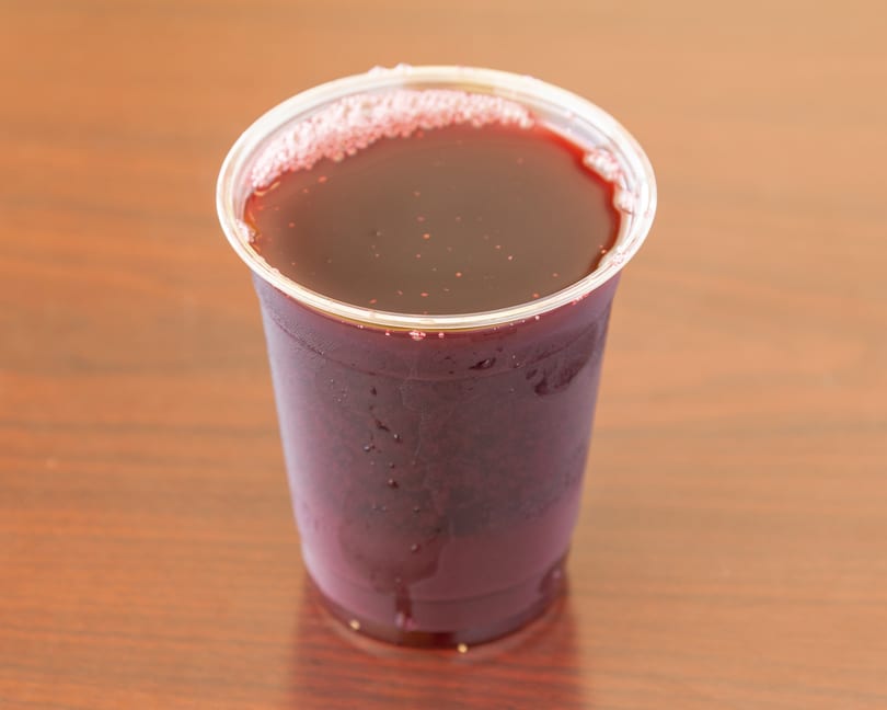 A clear plastic cup filled with a dark red beverage, possibly juice, on a wooden surface.